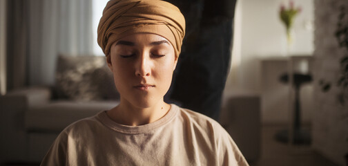 Young woman with cancer taking yoga and meditating in her apartment, banner. Strong female patient...