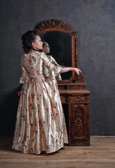 Beautiful woman in rococo style medieval dress standing near console mirror table and pull her hand