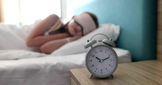 Woman or teenager sleeps on bed with an eye mask and 10 o'clock alarm clock. Morning sleep and awakening