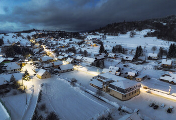 View of snowy mountain range and village with illuminated houses located at bottom of hill in Slovkia at sundown