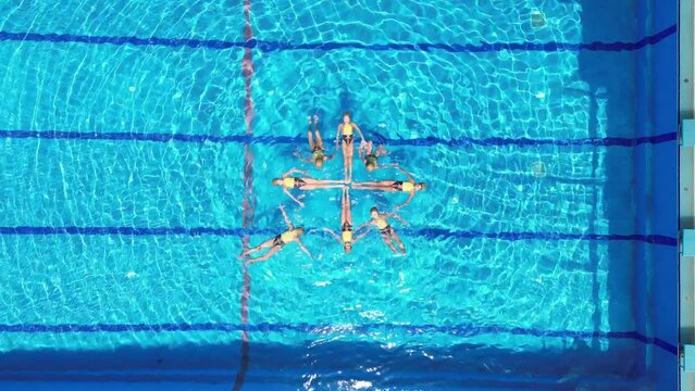 Aerial view of eight teenage girls learn figures in the pool. Girls learn competitive swimming in the pool. Team water sports. Synchronized swimming.