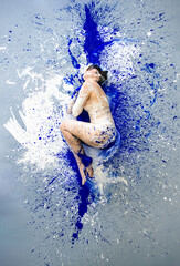 Young naked sexy woman in blue and white paint color painted, lies decorative sensual seductive in elegant pose on the colorful studio floor. Creative, abstract expressive bodypainting art