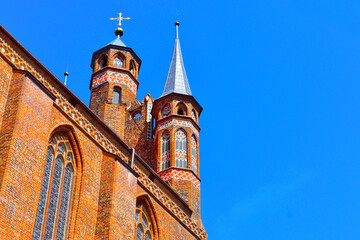 Fototapeta na wymiar Cathedral towers with a cross on top and red brick's wall of catholic church, in the background of blue sky. Sunny summer day. Poland, Torun, August 2023.