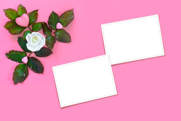 Beautiful white roses with green foliage and heart for Valentine's Day on pink paper background. Creative greeting card.
