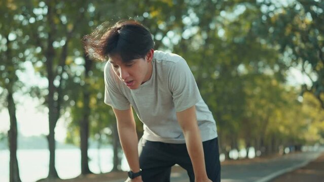 Tired runner asian man breathing after run marathon in public park. Young male athlete have break after running exercise in summer park. Sport man resting after workout outdoor.