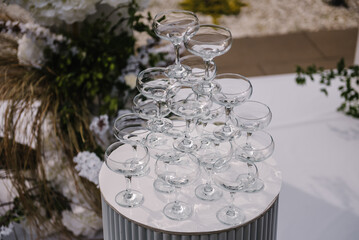 Pyramid of champagne glasses at a party. Location for celebration on pier. Wedding decor in banquet area. Ceremony is decorated flowers and greens in backyard. Wedding decorations in luxury ceremony.