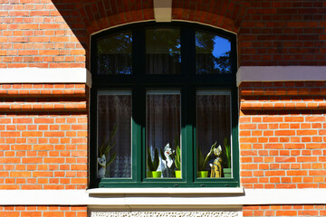Facade of the historic building with wide window, green dark frame,  the figures of cats outside the window and a red brick wall. Ancient architecture, old street. Torun, Poland, August 2023 