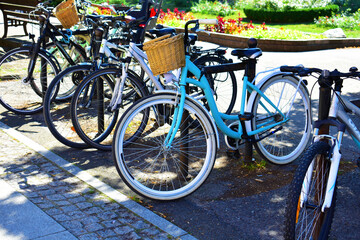Parked multicolored bicycles with wicker baskets near the greenery. Parking, street transport. Torun, Poland, August 2023  