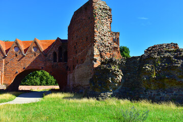 Old brick dilapidated wall and an arched passage under the path. Ruins of the fortress. Ancient building against a blue sky background and green lawn. Poland, Torun, August 2023. 