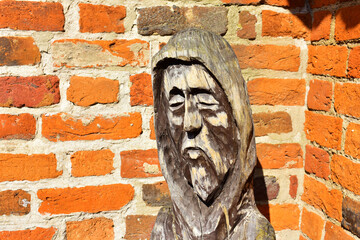 Wooden figure of a monk on the background of an old brick wall. Poland, Torun, August 2023.