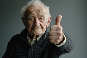 Elderly man happily giving a thumbs up on a gray background, age acceptance concept