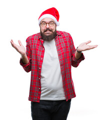 Young caucasian man wearing christmas hat over isolated background clueless and confused expression with arms and hands raised. Doubt concept.