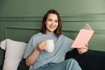 Smart, Happy Middle-aged Woman Enjoying Book and Tea, Relaxing in Spare Time. Intelligent Leisure. Young Woman Reading, Relishing Relaxation, and Sipping Tea