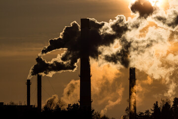 Silhouette of tall smoking factory tubes against the backdrop of the setting sun