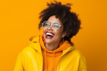 Portrait of a laughing african american woman in yellow jacket and sunglasses over yellow background