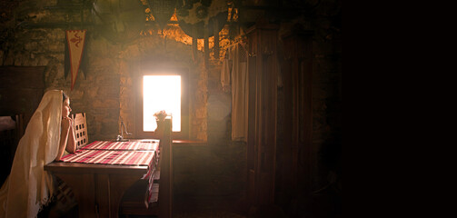 A girl sits at a table by the window in an ancient castle