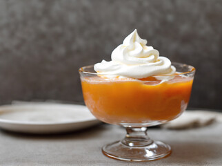 Delicious apricot dessert with whipped cream in glass on grey background