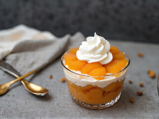 Delicious apricot dessert with whipped cream in glass on grey background