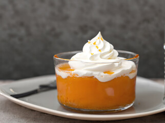 Delicious apricot dessert with whipped cream in glass on grey background