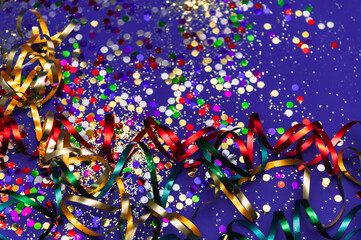 Multi-colored tinsel and confetti on a purple background. Festive, carnival background. Selective focus. Mardi Gras party, Venice Carnival.