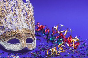 Golden Mardi Gras or carnival face mask on a purple background with colored tinsel and confetti....