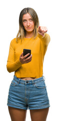 Young beautiful woman sending message using smartphone over isolated background pointing with finger to the camera and to you, hand sign, positive and confident gesture from the front