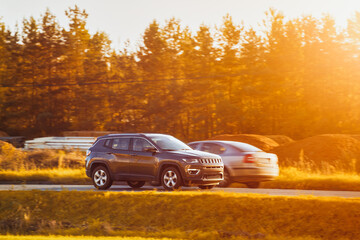 A subcompact SUV car explores the scenic countryside with a stunning sunset and alpine mountains in...