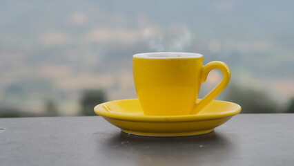 yellow coffee cup In the morning, a coffee cup is placed on the table in the background of a natural view.