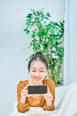 ルームウェアを着てスマートフォンの画面を見る若い女性