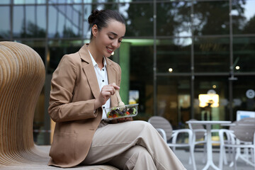 Happy young businesswoman eating lunch on bench outdoors