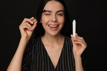 Obraz premium Beautiful young woman applying mascara on black background