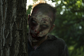 Scary zombie near tree outdoors. Halloween monster