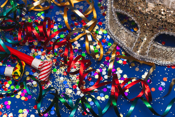 Golden Mardi Gras or carnival face mask  on a blue background with colored tinsel and confetti.Selective focus. - obrazy, fototapety, plakaty