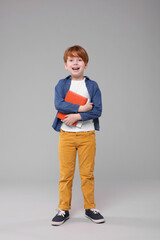 Happy schoolboy with books on grey background