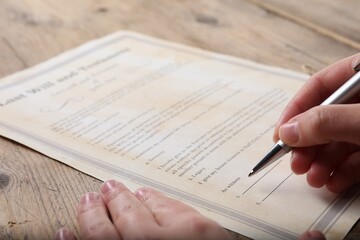 Woman signing Last Will and Testament at wooden table, closeup