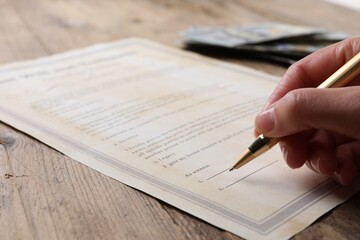 Woman signing Last Will and Testament at wooden table, closeup