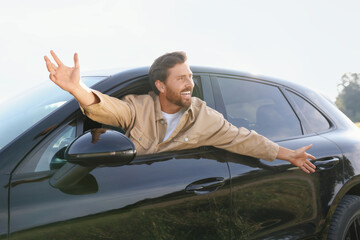 Enjoying trip. Happy man leaning out of car window outdoors