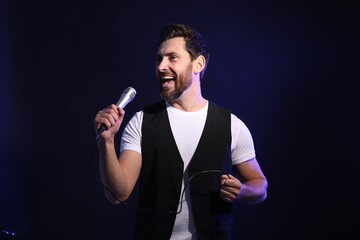 Naklejka premium Handsome man with microphone singing on dark blue background