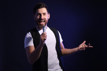 Handsome man with microphone singing on dark blue background