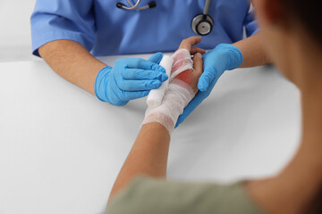 Doctor bandaging patient's burned hand at table, closeup