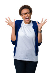 Naklejka premium Young beautiful african american woman wearing glasses over isolated background celebrating mad and crazy for success with arms raised and closed eyes screaming excited. Winner concept