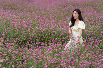 Fototapeta na wymiar beautiful woman in dress enjoying blooming pink globe amaranth or bachelor button field