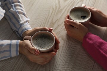 Women with cups of hot coffee at light wooden table, closeup