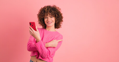 Young woman point to pink wall on pink background