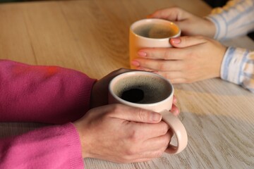 Women with cups of hot coffee at light wooden table, closeup