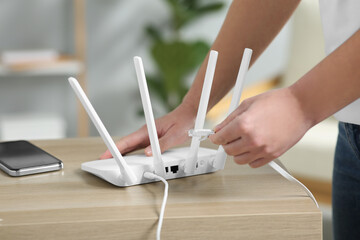 Woman inserting ethernet cable into Wi-Fi router at table indoors, closeup