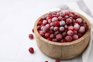 Frozen red cranberries in bowl on white tiled table, closeup. Space for text