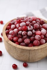 Frozen red cranberries in bowl on white table, closeup