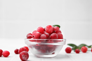 Frozen red cranberries in bowl on white table, closeup