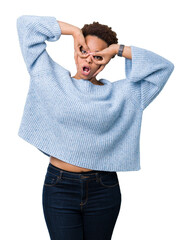 Young beautiful african american woman wearing a sweater over isolated background doing ok gesture like binoculars sticking tongue out, eyes looking through fingers. Crazy expression.